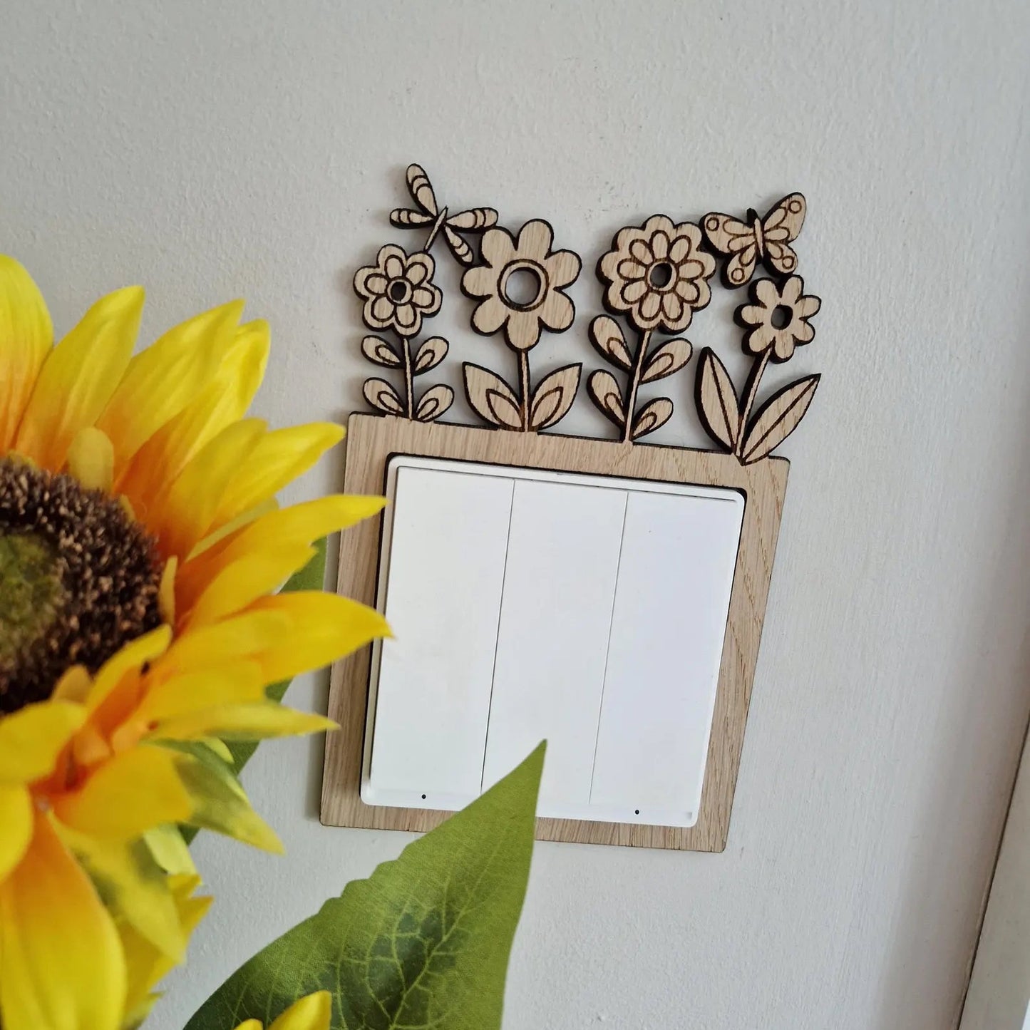 Decorative wall switch with floral design next to sunflowers on a white background