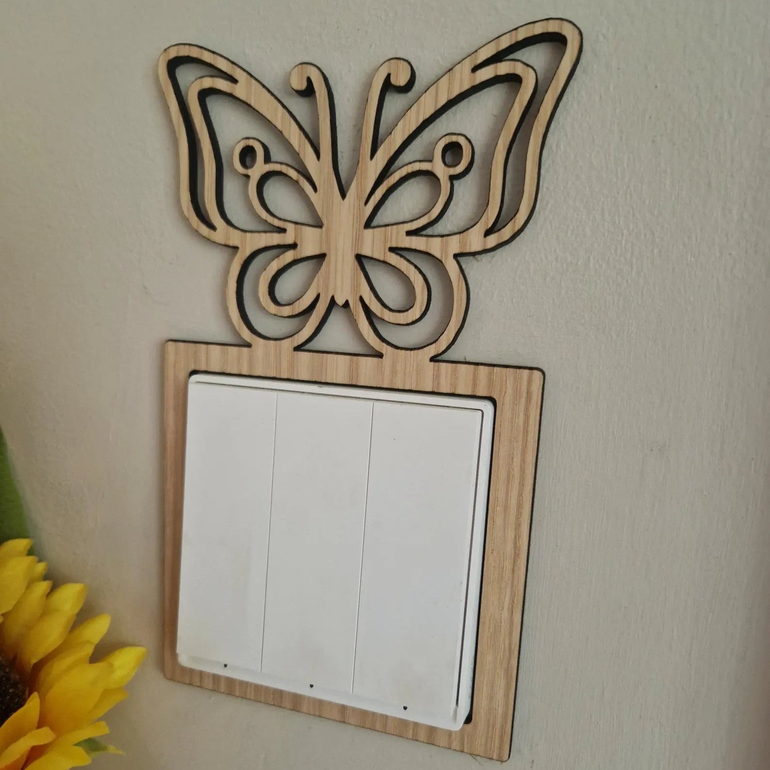 Wooden butterfly decorative switch plate on a wall with a sunflower in the corner.