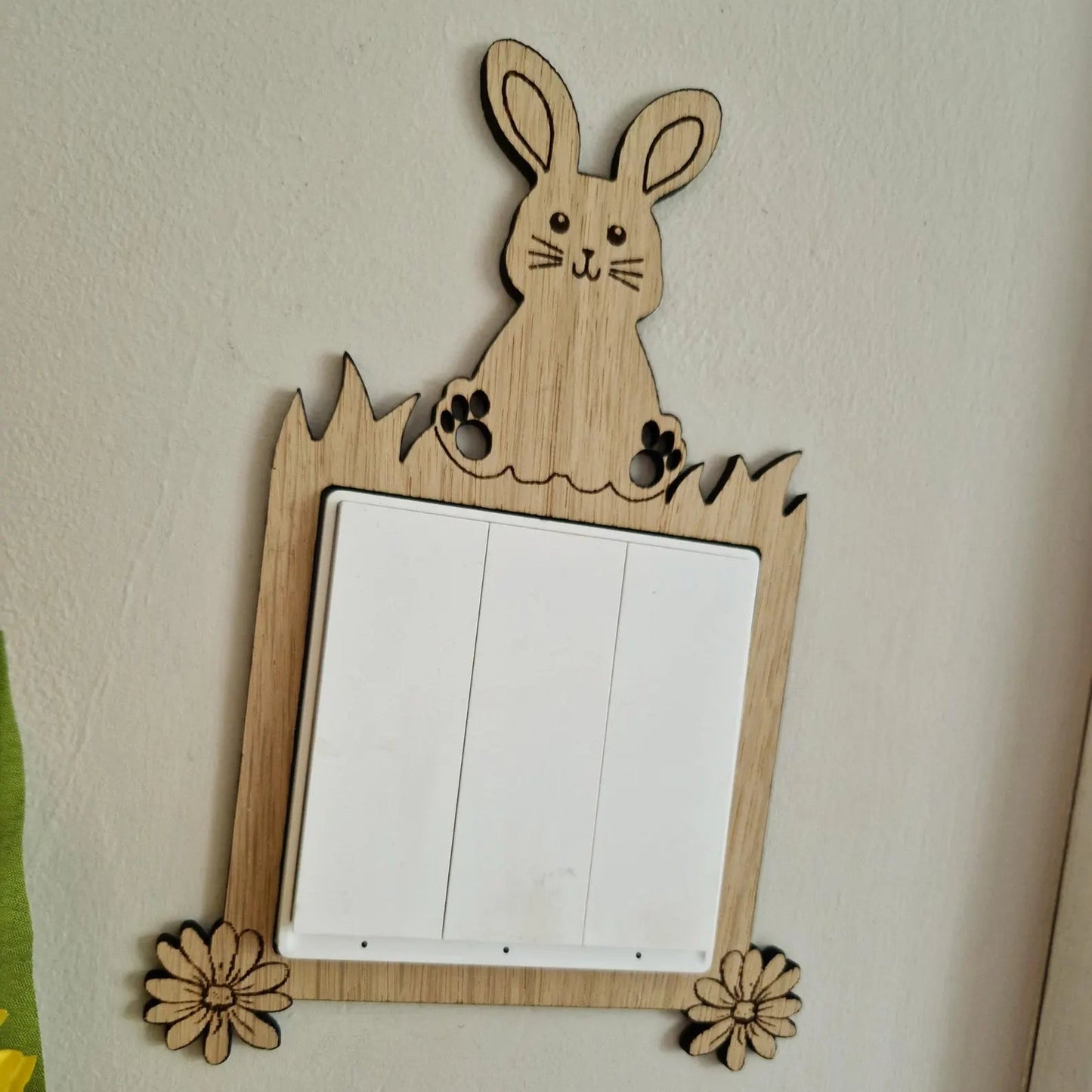 Wooden rabbit-shaped light switch cover on a wall with flowers in the foreground.