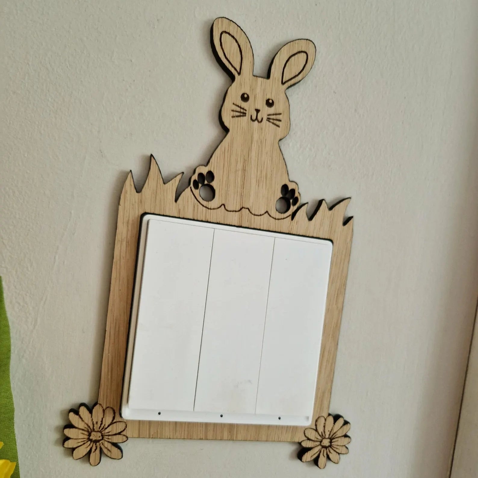 Wooden rabbit-shaped light switch cover on a wall with flowers in the foreground.