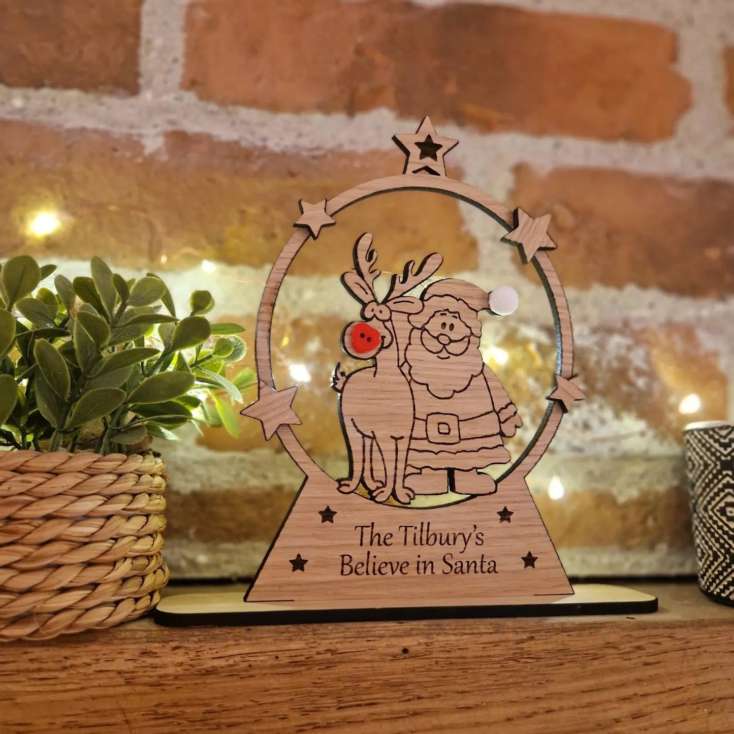 Wooden reindeer decoration with 'Believe in Santa' text on a wooden surface with a brick wall background.