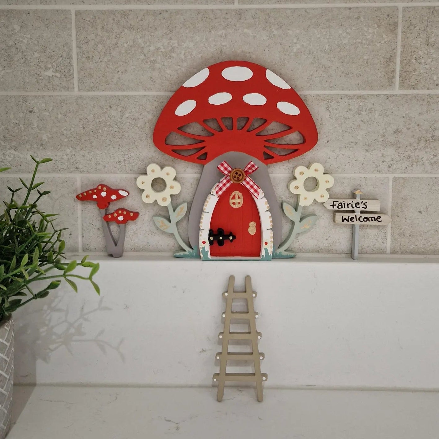 Decorative mushroom-shaped fairy door with a small ladder on a tiled wall.